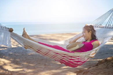 asian woman relaxing in the hammock on tropical beach, njoy her freedom and fresh air, wearing stylish hat and clothes. happy smiling tourist in tropics in travel vacation.
