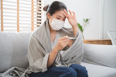 sick day at home in winter season. young asian woman have a fever checking thermometer and measure body temperature.