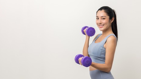 sporty asian woman exercises with dumbbells on isolated white background. good shape and health fitness woman weight training standing pose smile to camera.
