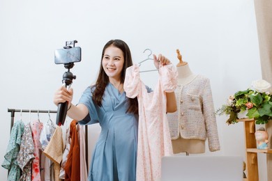 beautiful asia woman live streaming selling clothes online with smartphone at her shop. small business owner, online market concept.