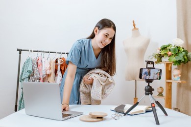 beautiful asia woman live streaming selling clothes online with smartphone at her shop. small business owner, online market concept.