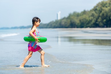 portrait of smiling asian child girl in swimwear running and playing on tropical beach in summer sunny day. happy little girl enjoy and fun outdoor activity lifestyle on travel vacation at the sea
