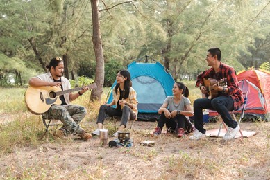 in the forest, asian male and female travelers are camping and partying, conversing, singing, and playing guitar.
