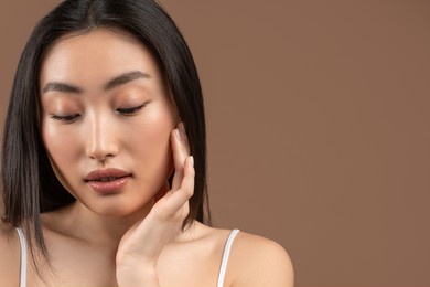 natural skincare. young pretty asian woman caressing her smooth soft skin with closed eyes, posing over brown background, copy space