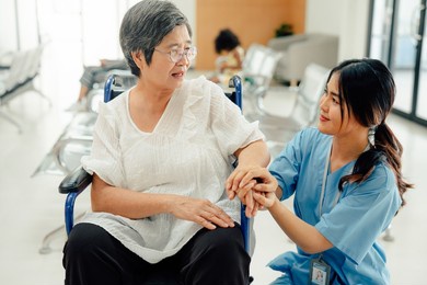 asian nurse taking care and talking mature female patient sitting on wheelchair in hospital. healthcare concept.