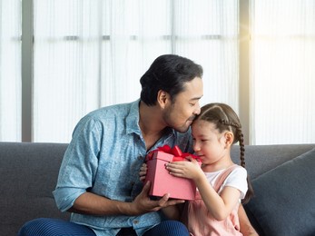 handsome asian father kisses on cute daughter's head after getting red box present. birthday, father's day or special day gift.