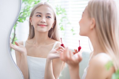 young asian woman applying lipstick in front of mirror
