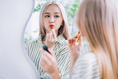young asian woman applying lipstick in front of mirror
