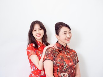 portrait of asian young daughter giving her mother a massage for relieve stress on white background(both wearing traditional cheongsam qipao dress).