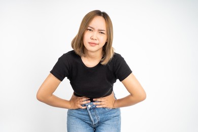 young asian woman having her period holding her stomach in pain on isolated background