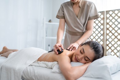 asian young relaxing woman getting back massage therapy with hot stone. attractive beautiful girl lying on massage table, getting physiotherapy from masseuse for skin and body care in spa beauty salon