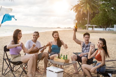 group of asian young man and woman having party on the beach together. attractive happy friends traveler singing and dancing while camping at seaside enjoy holiday vacation trip in tropical sea island