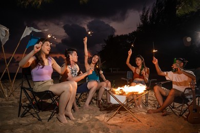 group of asian young man and woman having party on the beach at night. attractive friends traveler sing and dancing while camping at seaside enjoy holiday vacation trip in tropical sea island together