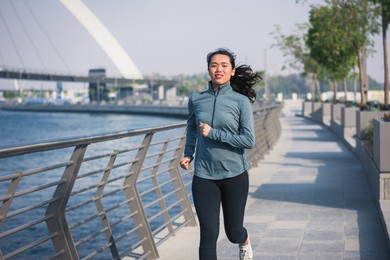 fit asian woman running in a modern city environment by the water on a promenade in dubai. jogging and healthy lifestyle abstract