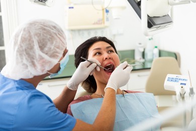 professional dentist man examining asian female patient teeth with dental tools - mirror and probe