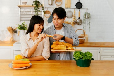 happiness asian couples tasting delicious homemade bread in the kitchen show their romantic relationship in the kitchen. have happy conversation and smile at each other.