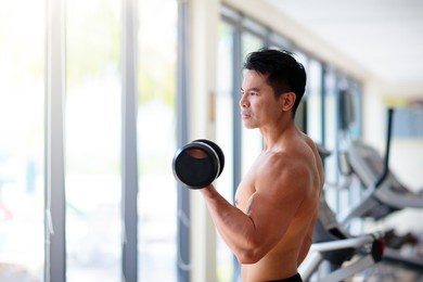 man exercising in gym. asian bodybuilder lifting weights. sport and healthy activity for young male. active chinese athlete in training. body building exercise work out.
