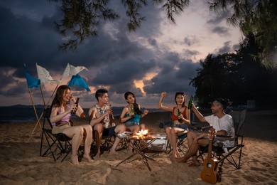 group of asian young man and woman having party on the beach at night. attractive friends traveler sing and dancing while camping at seaside enjoy holiday vacation trip in tropical sea island together