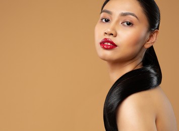 beauty face. brunette model with long black ponytail hairstyle. young asian woman with red lips and shining straight smooth hair over beige background. women facial and body skin care cosmetology