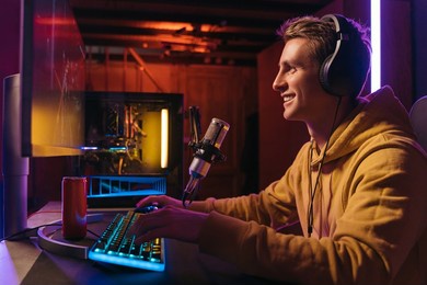  excited caucasian gamer streamer with headphones playing computer pc video at his living room, recording live stream using microphone, drinking energy drink. cyber sport and social media concept