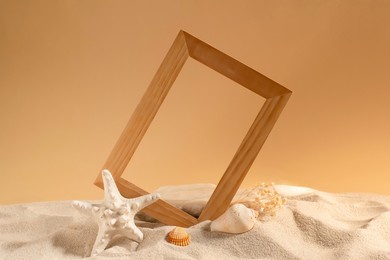 natural wooden frame inserted on the beach, with starfish and shells, to frame marine and summer themed products and concepts. concept of summer, warm light, and sand. horizontal format in the studio.