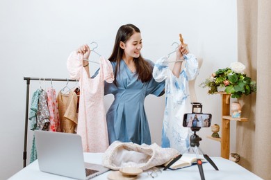 beautiful asia woman live streaming selling clothes online with smartphone at her shop. small business owner, online market concept.