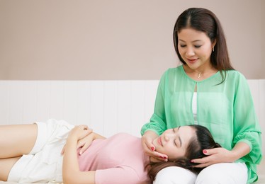 portrait of asian teenage daughter lies on her mother's lap on bed at home. the concept of caring, family relationships, trust, femininity. copy space