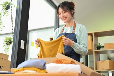attractive beautiful asian female clothes shop owner folding a t-shirt and packing in a cardboard parcel box. online fashion business.