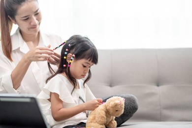 young asian mother tying daughter's hair