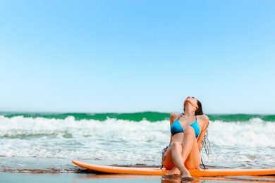 beautifull asian girl wearing bikini siting on surfboard and poses at the sand beach, in a tropical location, travel summer holiday relax in sea concept