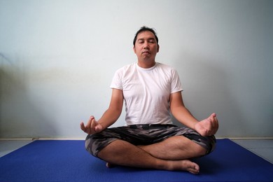 asian man in white shirt sitting yoga pose of happiness in his room at home
