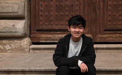 portrait of teenage asian boy sitting on stairway against building