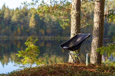 beautiful forest lake with camping folding chair, book and vacuum insulated bottle.