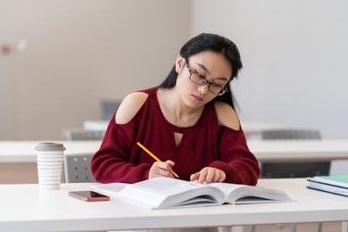 smart asian girl reading textbook and taking notes writing outline while preparing for exam, sitting in empty quiet university reading room or library, korean female student learning in classroom