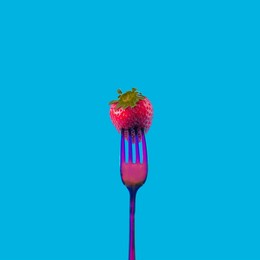 a fresh organic strawberry stacked on a neon colored flashy fork against blue background. vibrant minimal concept for seasonal fruits banner. artistic design for contemporary neon trend
