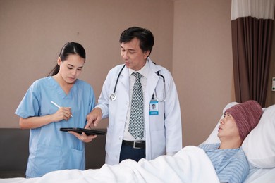 professional doctors team in uniform health check asian recovery male patient by stethoscope, medicine treatment at inpatient room bed in hospital ward, medical clinic, cancer examination consult.