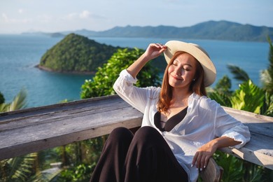 portrait image of a young asian woman sitting on resort terrace with a beautiful sea view