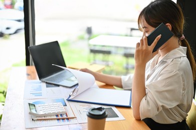 professional asian female office worker talking on the phone, calling her business supplier in the office.
