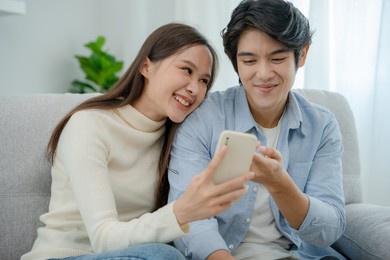 asian couples are enjoying new smartphones and online movies. young husband and wife after marriage. happiness and smiles and laughter in the family.