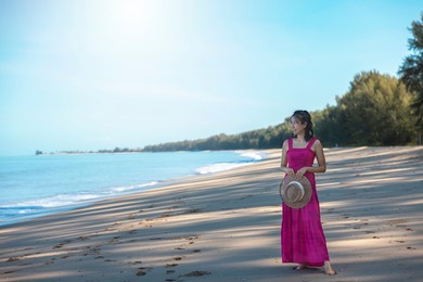 portrait beautiful traveller asian woman in pink dress enjoys relax smile leisure at beach by sea with blue sky in tropical beach vacation.