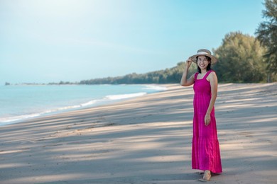 portrait beautiful traveller asian woman in pink dress enjoys relax smile leisure at beach by sea with blue sky in tropical beach vacation.