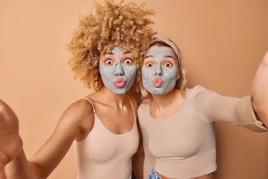 lovely young women make grimace at camera keep lips folded apply beauty clay mask to reduce fine lines dressed casually isolated over brown background. facial treatments and skin care concept