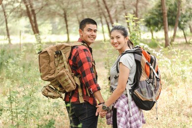 asian backpacker hiking couple holding hands looking at camera in forest.