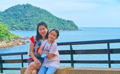 portrait of asian mother and little daughter travel at noen nangphaya viewpoint in  chanthaburi of thailand, middle-aged woman and child girl, blurred background sea, sky and island. daylight image.