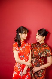young mother and daughter looking at each other standing in front of red background