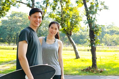 asian couple exercising together in the morning practice basic skateboarding on the streets of the park. playing sports for health makes you strong and happy.