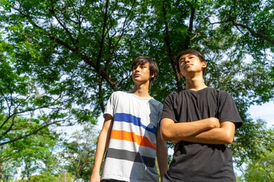 two young happy smiling teen boy standing in green park background.