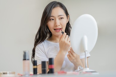 beauty cosmetics concept, hand of asian young woman, girl make up face by applying lipstick, lips balm on her mouth, looking at the mirror at home. female look with natural fashion style, skin care.
