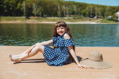a little girl sits on a pier near the city lake outdoors. summer vacation