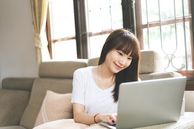 young adult asian woman stay at home with education time. university student relax learning via internet online technology by laptop computer. day time with window background.